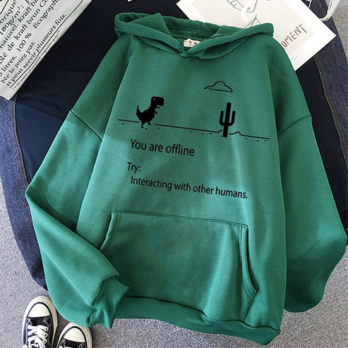 Groene hoodie met dinosaurus en cactus print, tekst "You are offline", op bed met spijkerbroek en sneakers. Trendy casual mode, comfortabele kleding.
