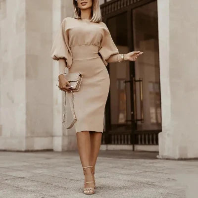 Elegante vrouw in beige jurk met pofmouwen en clutch, poseert voor moderne architectuur. Mode, stijlvol, chique outfit, stedelijke achtergrond.