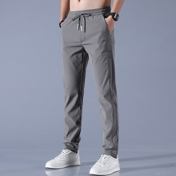 Grijze sportbroek voor heren met elastische tailleband en trekkoord, gecombineerd met witte sneakers. Comfortabele en stijlvolle vrijetijdskleding.