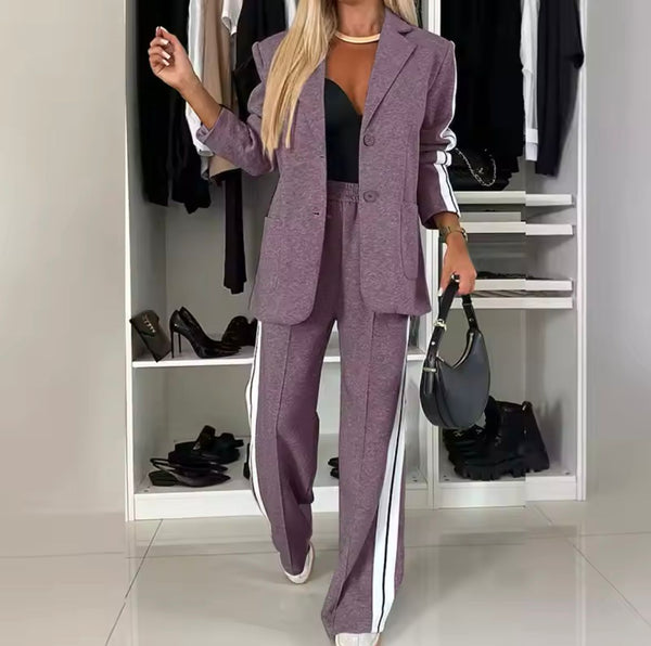 Vrouw in paarse blazer en broek met witte strepen, zwarte top en hakken, poseert voor kledingkast. Modieuze dameskleding, stijlvolle outfit.