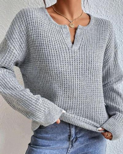 Grijze gebreide damestrui met V-hals, gedragen met blauwe jeans. Modieuze casual outfit, ideaal voor herfst- en winterseizoenen.