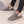 Grijze pluche pantoffels met witte voering, gedragen door persoon in zwarte jeans. Comfortabele winterse huisschoenen voor dames.