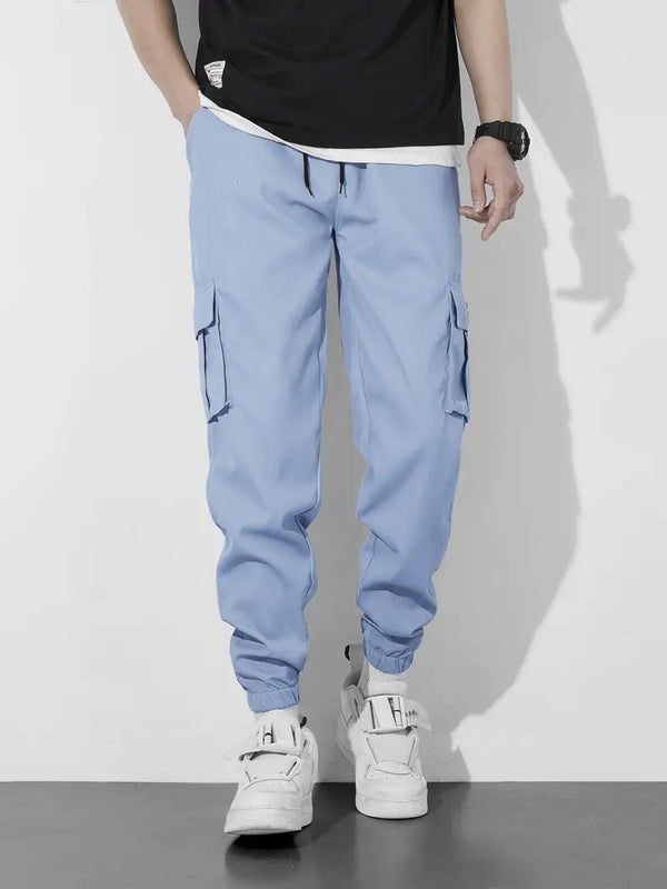 Man in lichtblauwe cargobroek en witte sneakers, casual mode, streetwear stijl, zwarte polshorloge, witte en zwarte t-shirt, trendy herenkleding.