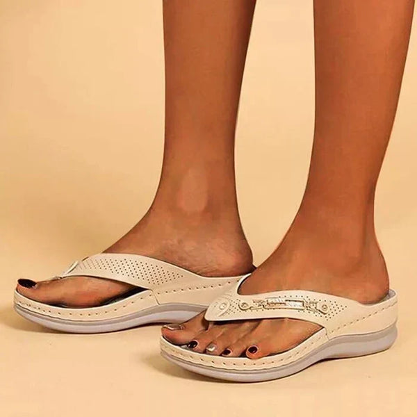 Vrouwelijke voeten in comfortabele, beige orthopedische slippers met verhoogde zool, ideaal voor dagelijks gebruik en ondersteuning van de voetboog.