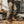 Man in beige cargobroek en bruine werkschoenen in een rustieke werkplaats met houtblokken en metalen kisten. Outdoor kleding, robuuste stijl.