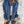Vrouw in blauwe corduroy jas met rits, witte top en zwarte jeans tegen betonnen muur. Modieuze dameskleding, casual herfstoutfit.