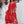 Vrouw in rode kaftan jurk met tie-dye patroon, staand voor witte muur met bloemen. Zomermode, bohemian stijl, comfortabele dameskleding.