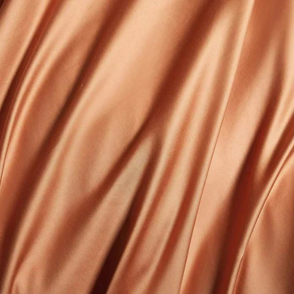 Zijdeachtige, glanzende stof in warme koperkleur, met vloeiende plooien. Luxe textiel, perfect voor mode en interieurdecoratie.