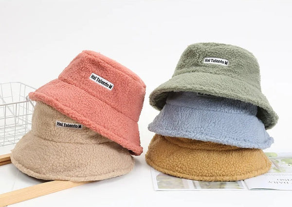 Vier kleurrijke, zachte teddy bucket hats gestapeld, met labels "Hai Talento M". Modieuze hoeden voor herfst en winter, trendy accessoires.