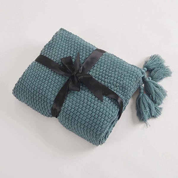 Gevouwen blauwe gebreide deken met zwarte strik en kwastjes, ideaal voor interieurdecoratie en comfort. Perfect als cadeau of woonaccessoire.