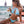 Vrouw in blauwe bikini met gevlochten haar drinkt sap op strand, zittend op ligstoel met zeezicht. Zomermode, strandvakantie, tropische sfeer.