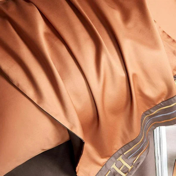 Zijdeachtige bruine en oranje sjaal met gouden letters, luxe modeaccessoire, elegant design, hoogwaardige stof, stijlvolle uitstraling.