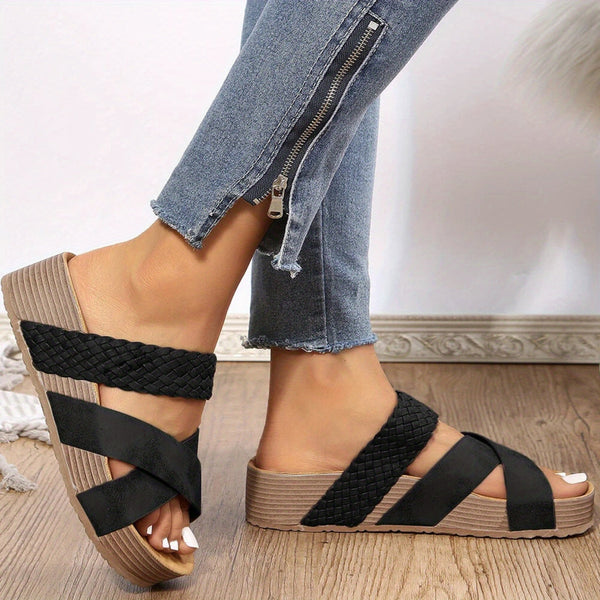 Zwarte gevlochten sandalen met sleehak, gedragen door een persoon in blauwe jeans met ritsdetail. Comfortabele zomerschoenen voor dames.