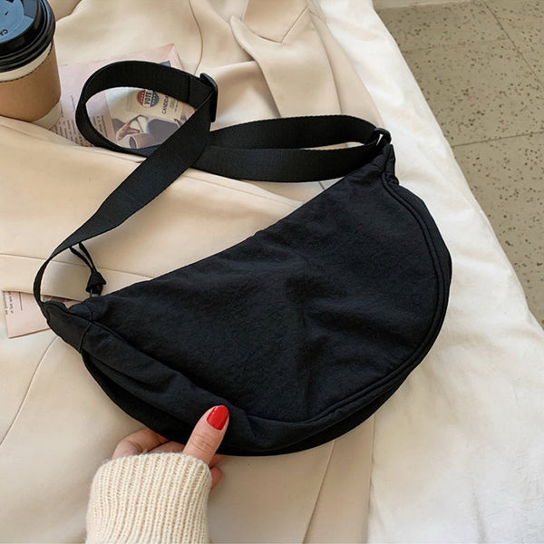 Zwarte schoudertas op beige jas, met verstelbare riem en ritssluiting. Perfect voor dagelijks gebruik. Stijlvolle en praktische accessoire.