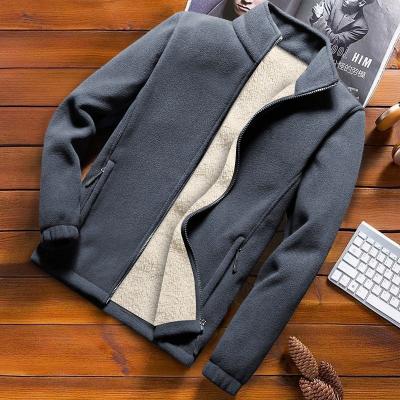 Donkergrijze fleece jas met ritssluiting en beige voering, liggend op houten tafel naast toetsenbord en tijdschrift. Wintermode, herenkleding.