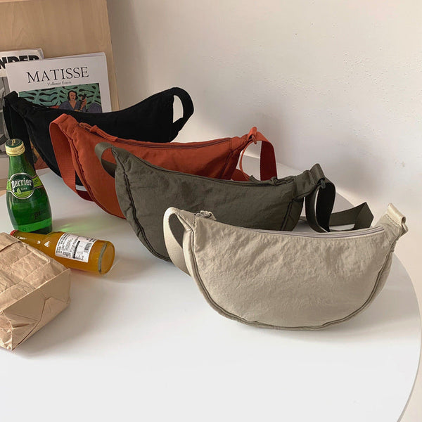 Vier crossbody tassen in beige, groen, oranje en zwart op een tafel met tijdschriften en drankjes. Stijlvolle en praktische schoudertassen.