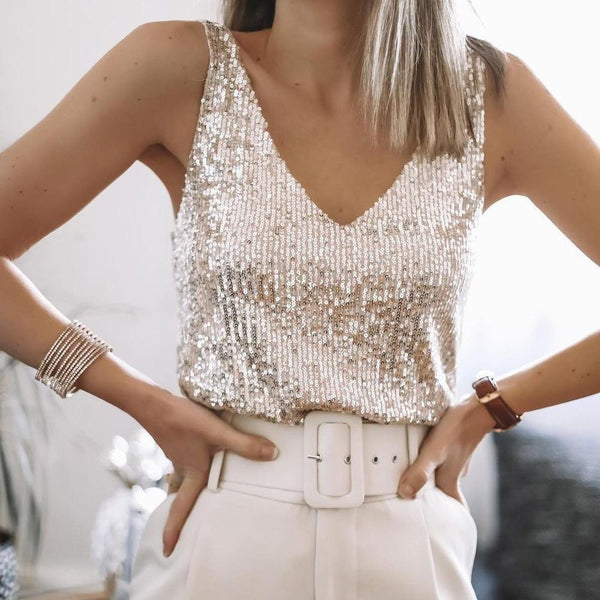 Vrouw in glinsterende pailletten top, witte broek met brede riem, armband en horloge. Modieuze dameskleding, feestelijke outfit.
