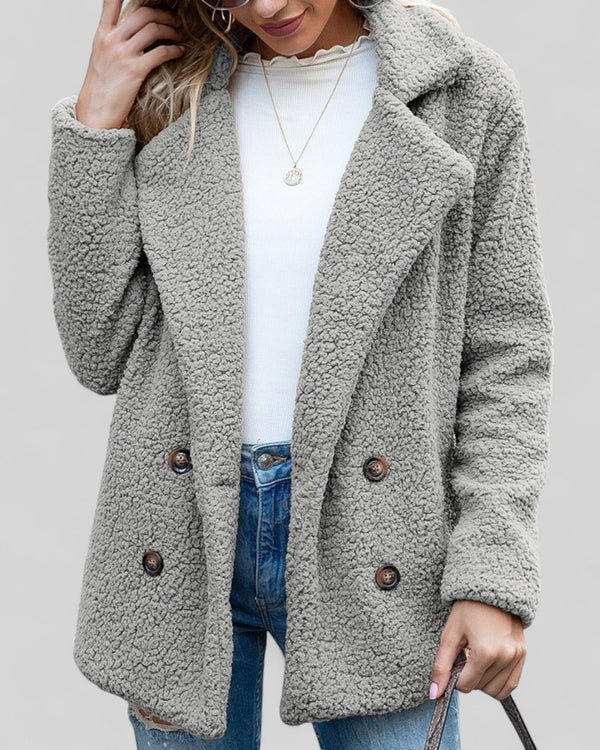 Grijze teddyjas voor dames, dubbelrij knopen, casual wintermode, gecombineerd met witte trui en spijkerbroek. Perfect voor koude dagen.