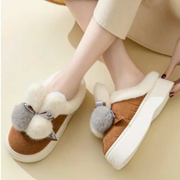 Bruine damespantoffels met witte voering, pompons en strikjes, comfortabele wintermode, warme huisschoenen, trendy en stijlvol design.