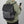 Persoon met groene hoodie draagt een stijlvolle, grijze rugzak met USB-oplaadpoort en ritsvakken, terwijl hij een smartphone vasthoudt.