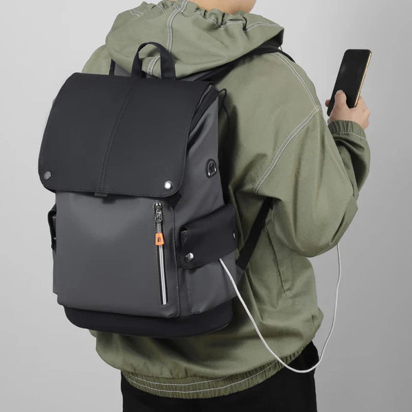 Persoon met groene hoodie draagt een stijlvolle, grijze rugzak met USB-oplaadpoort en ritsvakken, terwijl hij een smartphone vasthoudt.