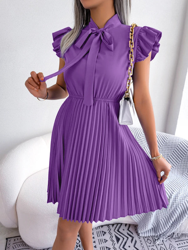 Vrouw in paarse geplooide jurk met strik, gouden kettingtas, moderne mode, elegante kleding, trendy outfit, stijlvolle dameskleding.