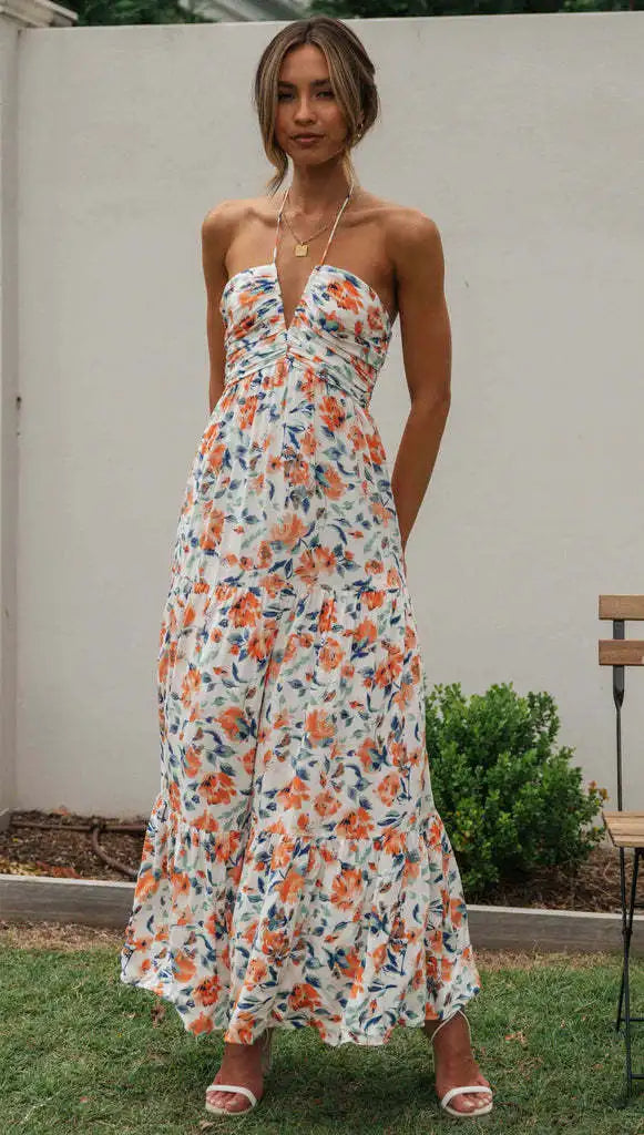 Vrouw in lange, strapless bloemenjurk met oranje en blauwe patronen, staand in tuin. Zomermode, elegante dameskleding, casual stijl.