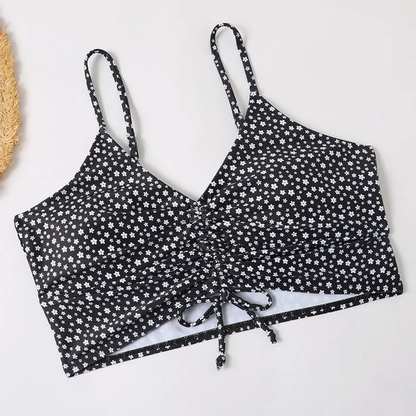 Zwarte crop top met witte bloemenprint, verstelbare bandjes en strikdetail. Trendy dameskleding, perfect voor zomeroutfits en casual stijlen.