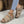 Beige dames sandalen met gevlochten bandjes en sleehak, gedragen met kleurrijke enkelband, op een lichte vloer. Perfect voor zomerse casual outfits.