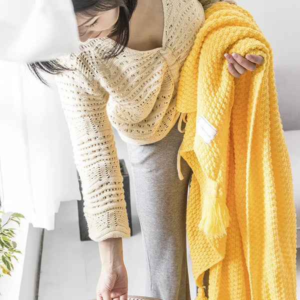 Vrouw met gebreide trui houdt gele deken vast in lichte woonkamer. Gezellig interieur, moderne woondecoratie, comfortabele textiel.