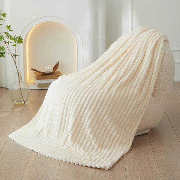 Crèmekleurige geribbelde deken op moderne fauteuil, minimalistisch interieur, houten vloer, decoratieve vaas, stijlvolle woonaccessoires.