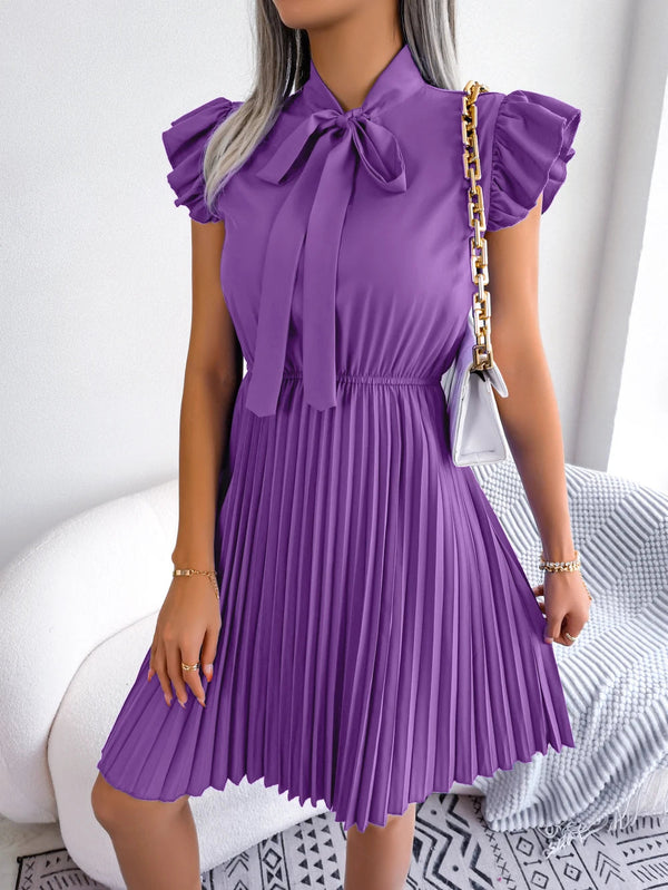 Vrouw in paarse geplooide jurk met strik, gouden kettingtas, moderne mode, elegante outfit, trendy kleding, stijlvolle dameskleding.