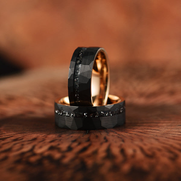Twee zwarte tungsten trouwringen met facetten en gouden binnenkant, geplaatst op een houten oppervlak. Luxe, moderne trouwringen voor koppels.