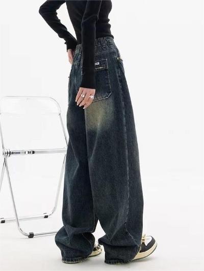 Model draagt wijde, donkere spijkerbroek met vintage look, gecombineerd met zwarte top en sneakers. Trendy streetwear mode voor dames.