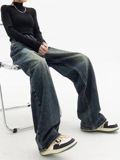 Vrouw in zwarte trui en wijde jeans zittend op een stoel, met retro sneakers. Modieuze casual outfit, streetwear stijl.