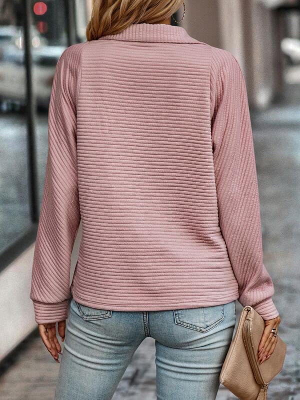 Vrouw in roze geribbelde trui en blauwe jeans, rugaanzicht, met beige clutch. Modieuze dameskleding, casual herfstoutfit, stedelijke achtergrond.