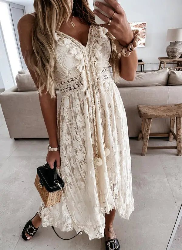 Vrouw in elegante witte kanten jurk met V-hals en pompons, poseert in moderne woonkamer. Zomerjurk, boho-stijl, modieuze outfit, casual chic.