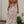 Vrouw in lange, bloemenjurk met blote rug, staand in tuin. Zomerse mode, elegante stijl, kleurrijk bloemenpatroon, casual chique uitstraling.