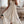 Vrouw in elegante, witte kanten zomerjurk met pompons, staand in moderne woonkamer. Perfecte boho-chic outfit voor zomerse dagen.