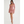 Vrouw in roze, asymmetrische mini-jurk met lange mouwen en cut-out detail, poseert tegen witte achtergrond. Trendy damesmode, elegante avondkleding.