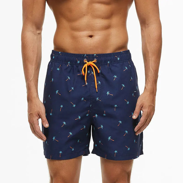 Donkerblauwe zwembroek met palmbomenprint en oranje trekkoord, gedragen door man. Perfect voor strandmode en zomerse zwemkleding.