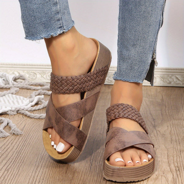 Vrouwelijke voeten in bruine gevlochten sandalen op houten vloer, gecombineerd met blauwe jeans. Modieuze zomerschoenen, casual stijl.