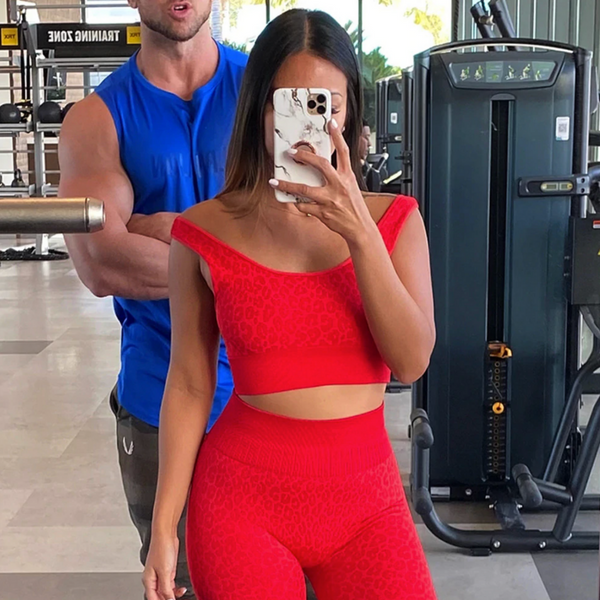 Vrouw in rode sportkleding maakt selfie in sportschool met fitnessapparatuur op de achtergrond. Fitness, sportkleding, sportschool, selfie.