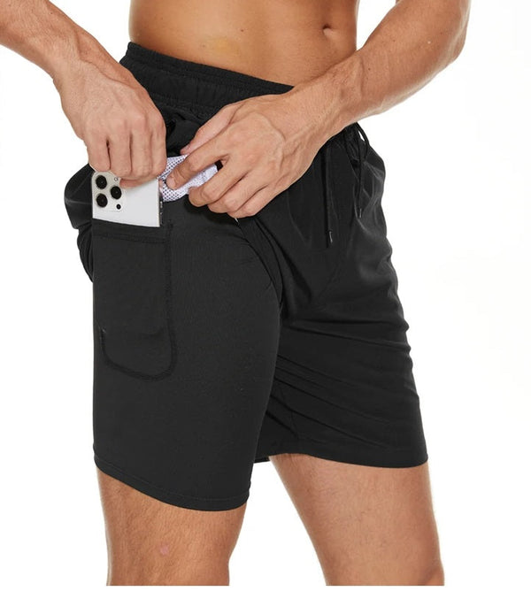 Man in zwarte sportshorts met telefoon in zijzak, elastische tailleband, geschikt voor hardlopen en fitness. Comfortabele en functionele sportkleding.