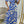 Vrouw in blauwe en beige off-shoulder maxi-jurk met zebraprint, poseert voor spiegel in moderne kamer. Trendy zomerjurk, mode, dameskleding.