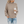 Vrouw in beige gebreide trui met koffiebeker, casual herfstmode, gescheurde jeans, grijze achtergrond. Trendy dameskleding, comfortabele stijl.