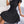 Elegante zwarte plissé jurk met strikdetail, gedragen door zittende vrouw op bank. Perfect voor modieuze dameskleding en stijlvolle outfits.