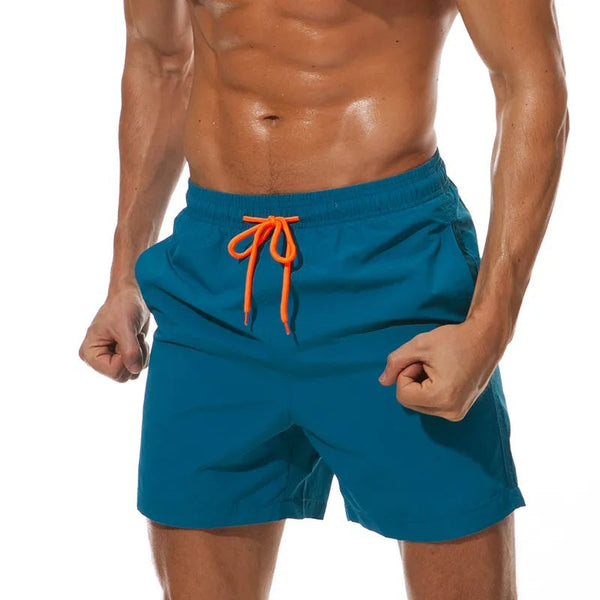 Man in blauwe zwembroek met oranje koord, gespierde torso, strandkleding, zomermode, sportieve zwemshorts, herenbadmode.