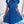 Vrouw in elegante blauwe plisséjurk met strik, korte mouwen, staande in moderne kamer. Mode, dameskleding, stijlvolle jurk, trendy outfit.
