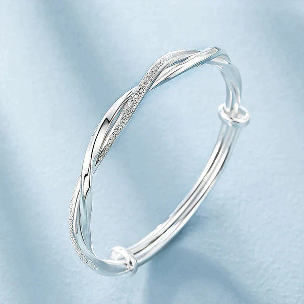 Zilveren armband met gedraaide, gevlochten details op een lichtblauwe achtergrond. Elegant sieraad, perfect voor damesmode en cadeau-ideeën.